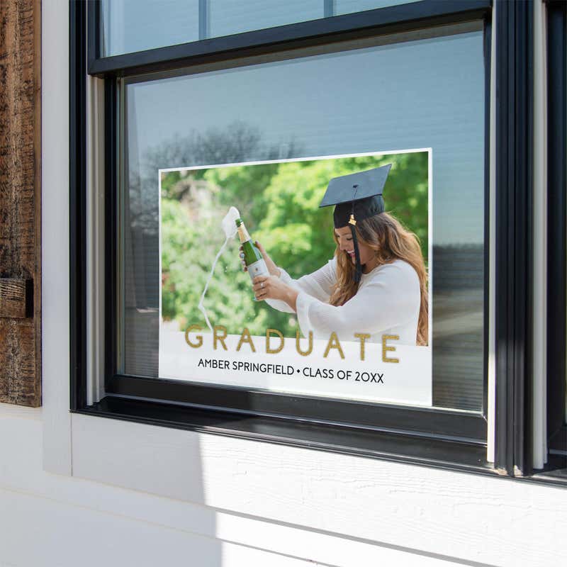 Gold text graduation yard sign displayed in a window