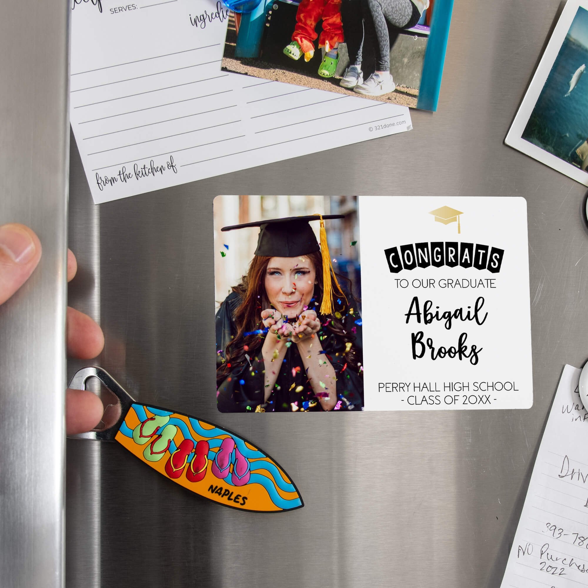 Hand placing a custom Congrats to Our Grad Graduation Announcement magnet on a stainless steel refrigerator