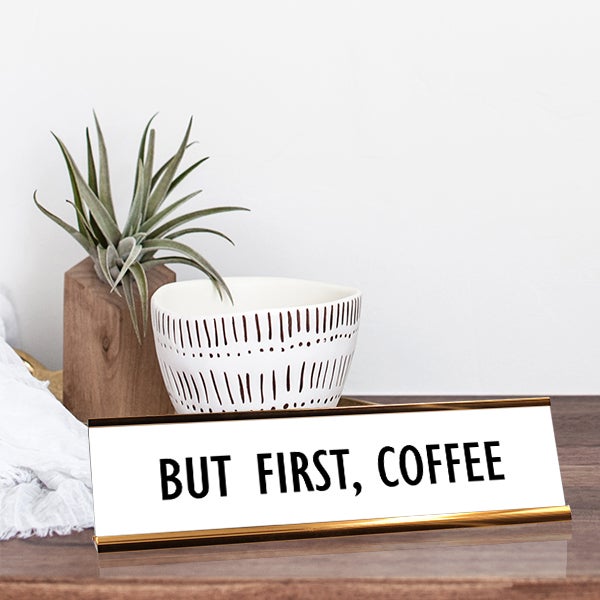 White desk plate with black custom text in yellow gold holder on a desk