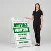 Woman standing beside a drivers wanted A-frame sign for scale