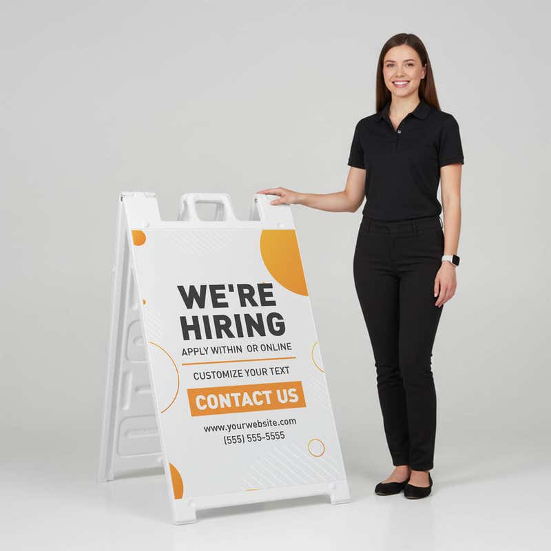 Woman standing beside a orange now hiring A-frame sign for scale