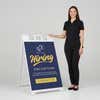 Woman standing beside a blue now hiring A-frame sign for scale