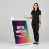 Woman standing beside a rainbow now hiring A-frame sign for scale