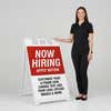 Woman standing beside a red now hiring A-frame sign for scale