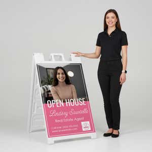 Woman standing beside a pink open house A-frame sign for scale