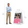 Pink open house A-frame sign shown with size dimensions beside a man