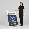Woman standing beside a logo parking A-frame sign for scale