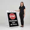 Woman standing beside a parking lot full A-frame sign for scale