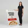Woman standing beside a special offer A-frame sign for scale
