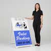 Woman standing beside a valet parking A-frame sign for scale