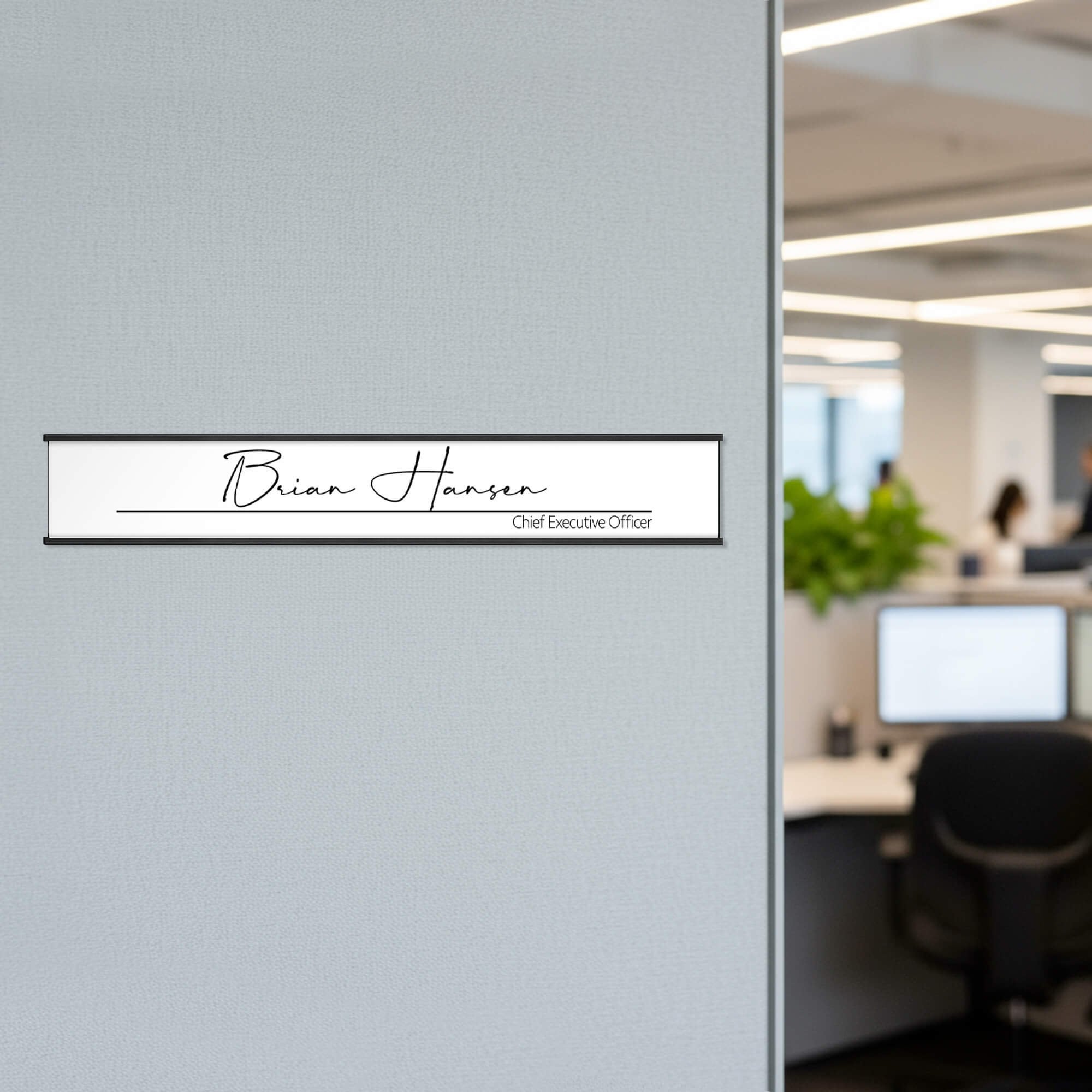 A white name plate with a black aluminum holder on an office wall