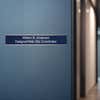 A blue name plate with a silver aluminum wall holder on an office door