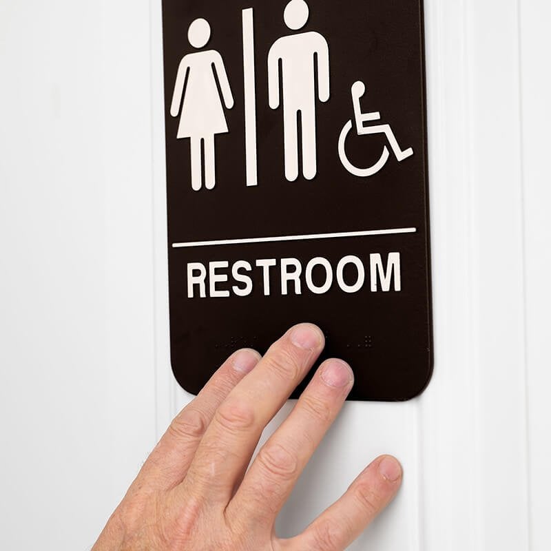 Someone feeling the braille on a 9 x 6 restroom sign