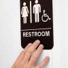 Someone feeling the braille on a 9 x 6 restroom sign