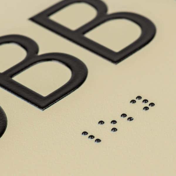 A close-up on the braille and tactile text on the ADA sign