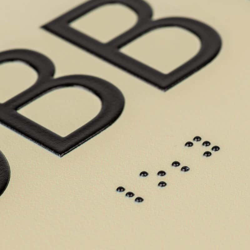 A close-up on the braille and tactile text on the ADA sign