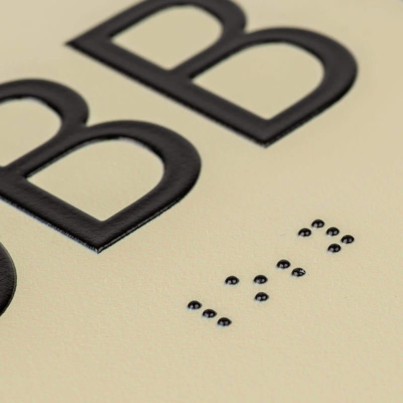 A close-up on the braille and tactile text on the ADA sign