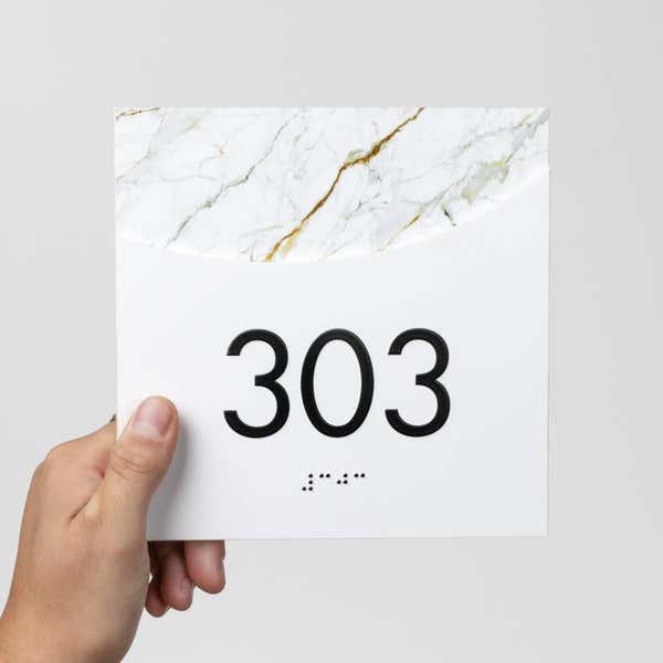 A person holding a modern arch 2-layer sign with a room number on it
