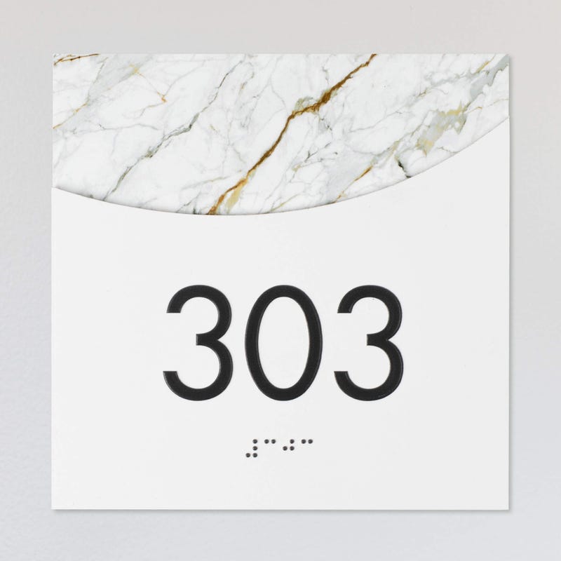 A layered ADA sign for a room number with a white foreground and the white marble background