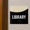 A 2-layered ADA sign for a library with a black foreground and modern geometric background