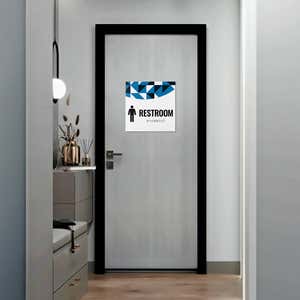 A 2-layered ADA sign for a restroom with a white foreground and a blue geometric background
