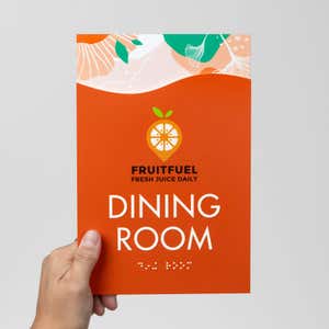 A person holding an orange 2-layer modern ADA sign for a dining room