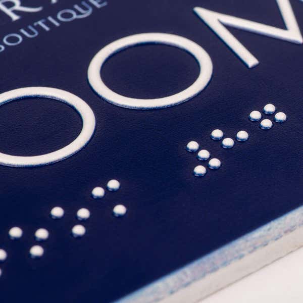 A close-up on the tactile text and braille on the modern sleek 2-layer ADA sign