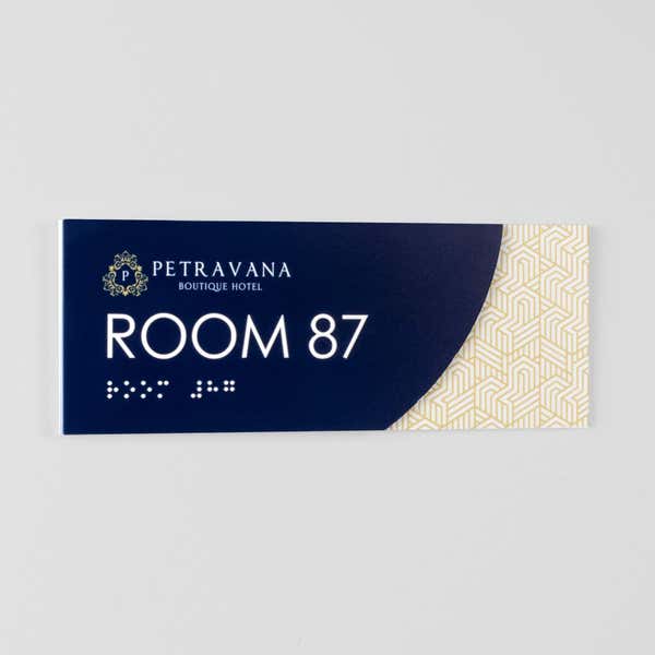 A 2-layered ADA sign for a room mounted on a plain white wall