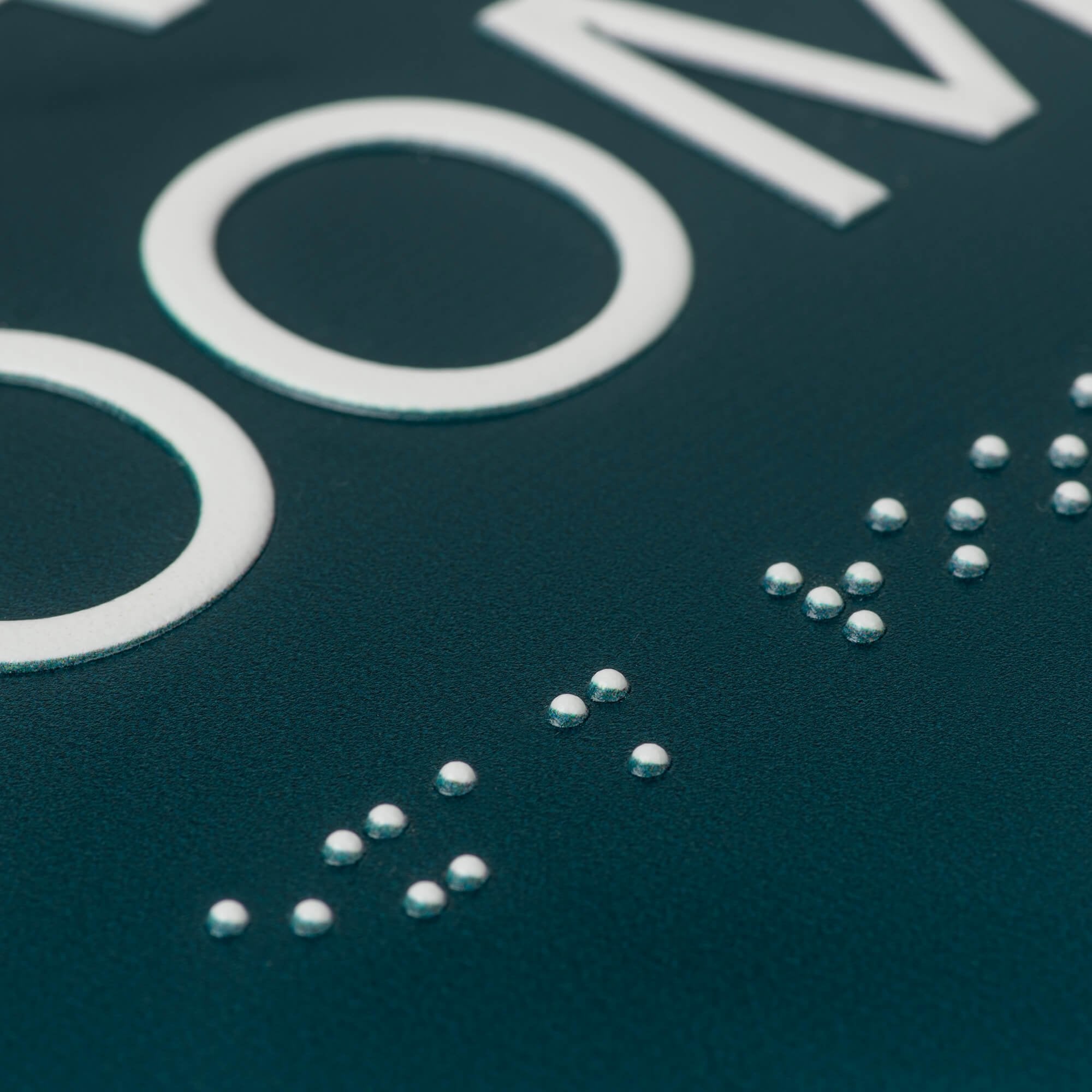 A close-up on the tactile text and braille for the 2-layered round ADA sign A close-up on the tactile text and braille for the 2-layered round ADA sign