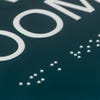 A close-up on the tactile text and braille for the 2-layered round ADA sign