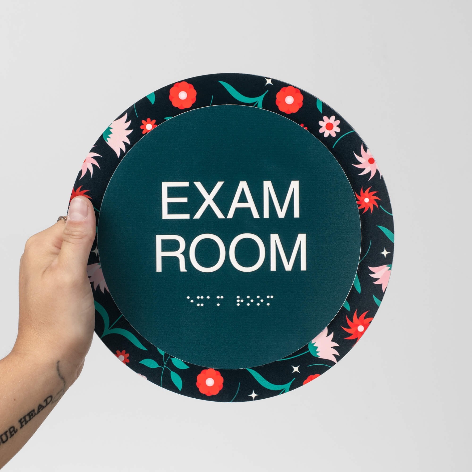 A person holding a round 2-layered ADA sign that says "exam room" A person holding a round 2-layered ADA sign that says "exam room"