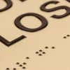 A close-up of the tactile letters and braille on the two-tone layered ADA sign