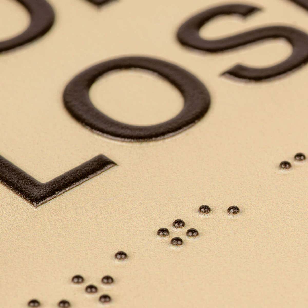 A close-up of the tactile letters and braille on the two-tone layered ADA sign