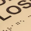 A close-up of the tactile letters and braille on the two-tone layered ADA sign