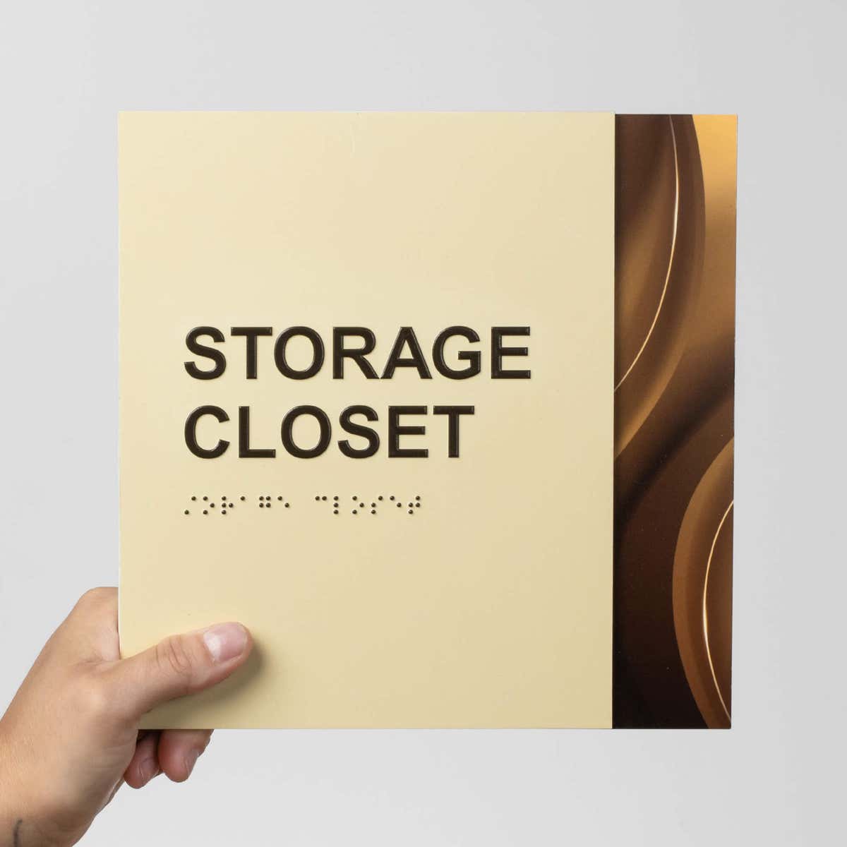 A person holding a two-tone layered ADA sign that says "storage closet"
