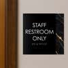 A modern layered ADA sign for a staff restroom hung next to a doorway