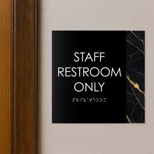 A modern layered ADA sign for a staff restroom hung next to a doorway