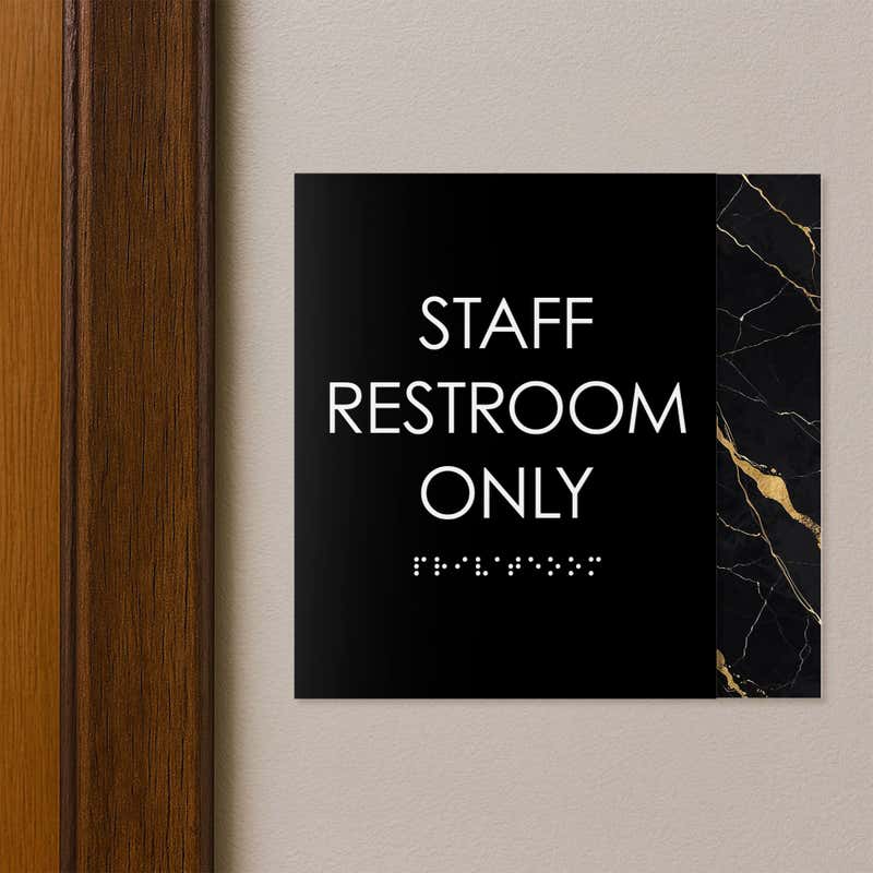 A modern layered ADA sign for a staff restroom hung next to a doorway