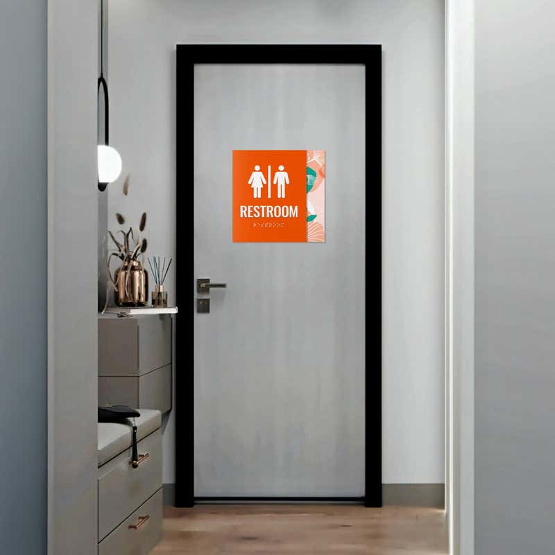 A large 2-layered ADA sign with an orange foreground and floral background for a restroom