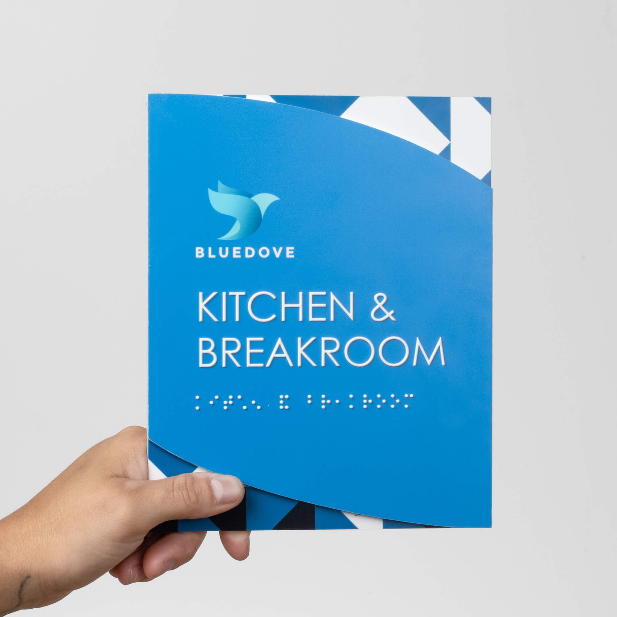 Someone holding the modern twist ADA sign with a blue geometric background and baby blue foreground