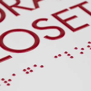 A close-up on the braille and tactile text of the ADA sign