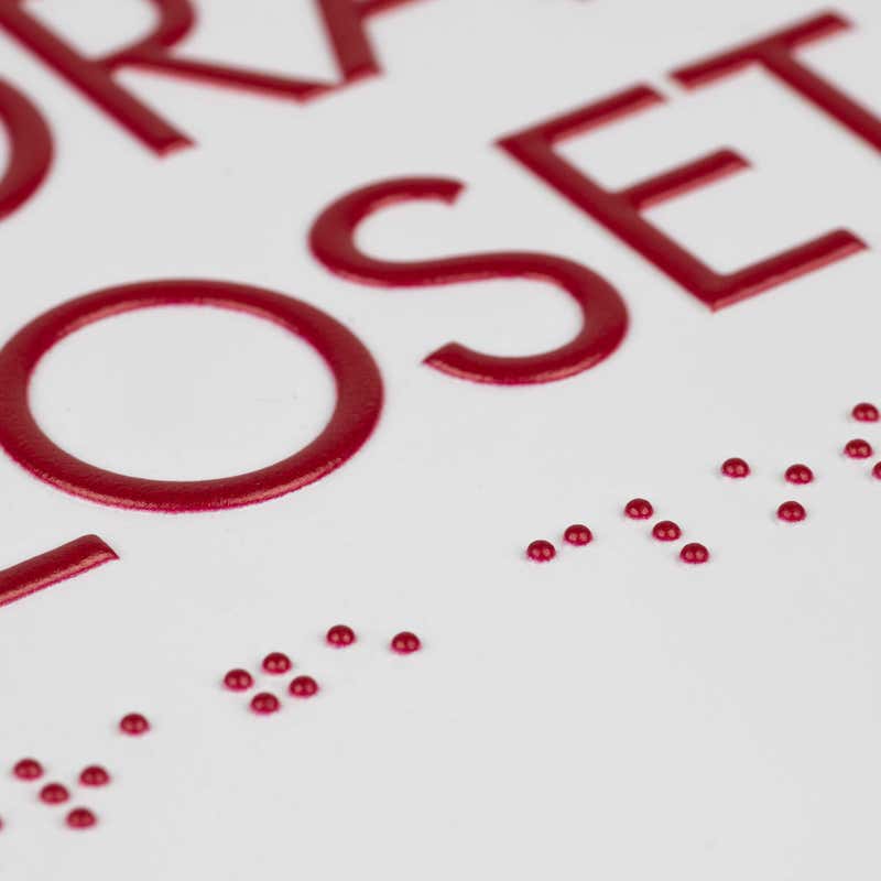 A close-up on the braille and tactile text of the ADA sign