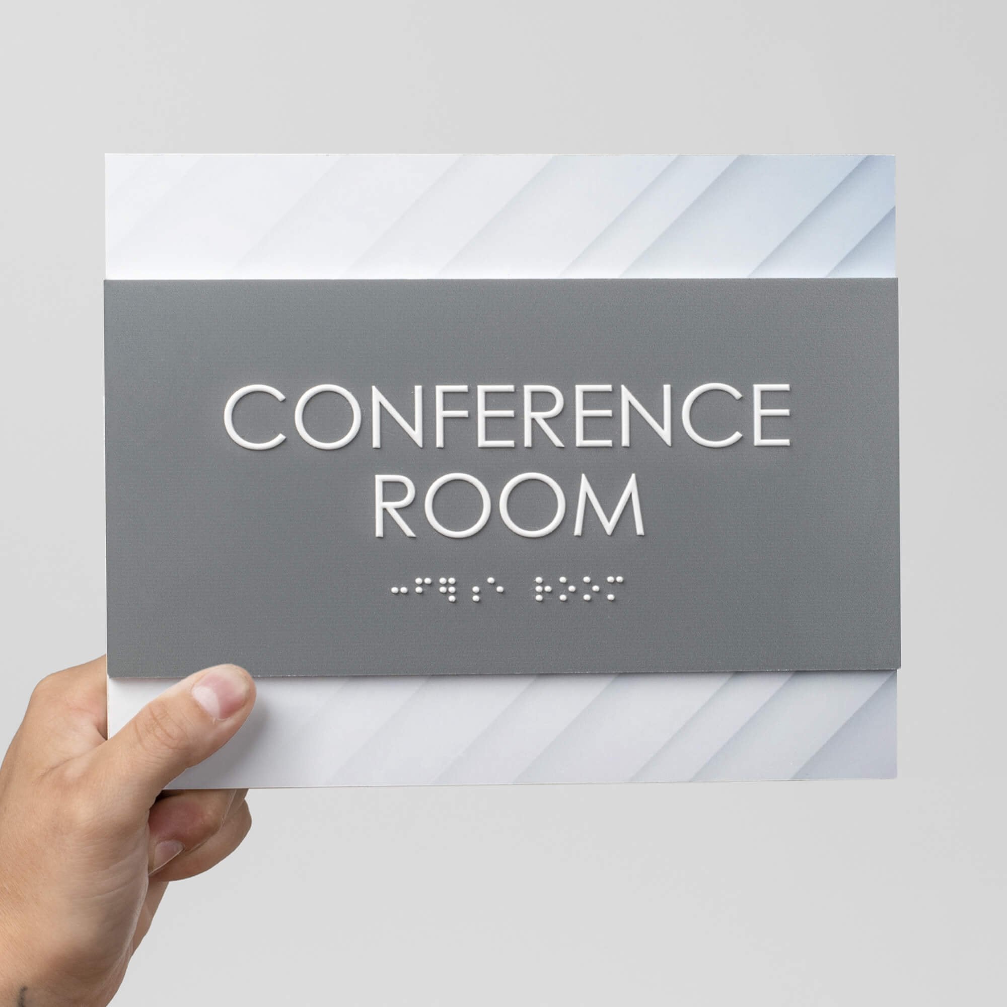 A person holding a 2-layered ADA sign for a conference room with a gray foreground and minimal diagonal background A person holding a 2-layered ADA sign for a conference room with a gray foreground and minimal diagonal background