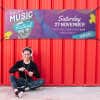 Purple outdoor vinyl banner with bold event typography and graphic design elements, mounted on a red corrugated wall