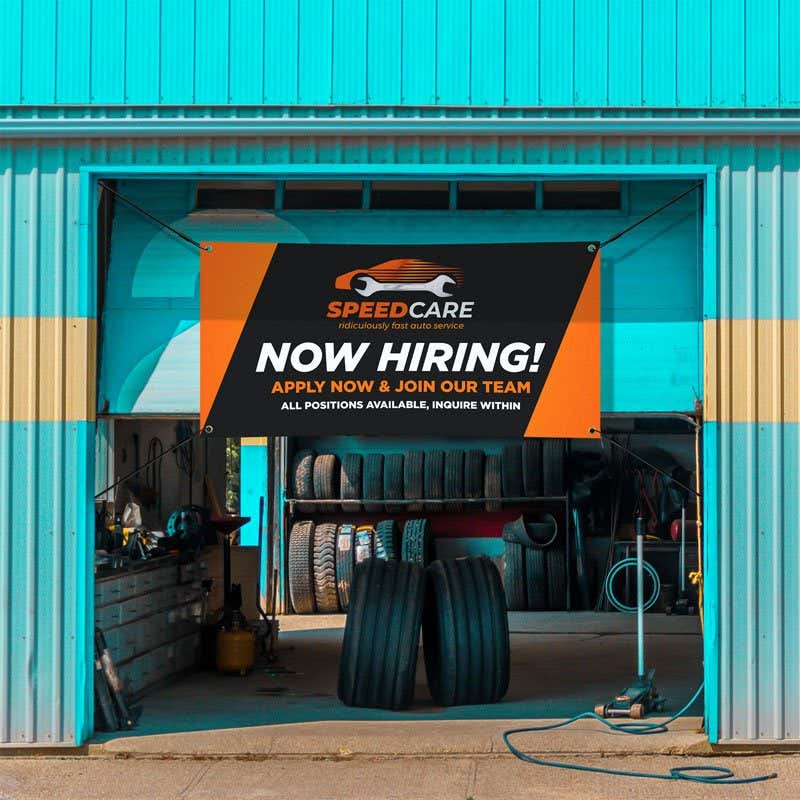 Black and orange outdoor vinyl banner with bold business branding and text, hanging in an auto shop garage doorway
