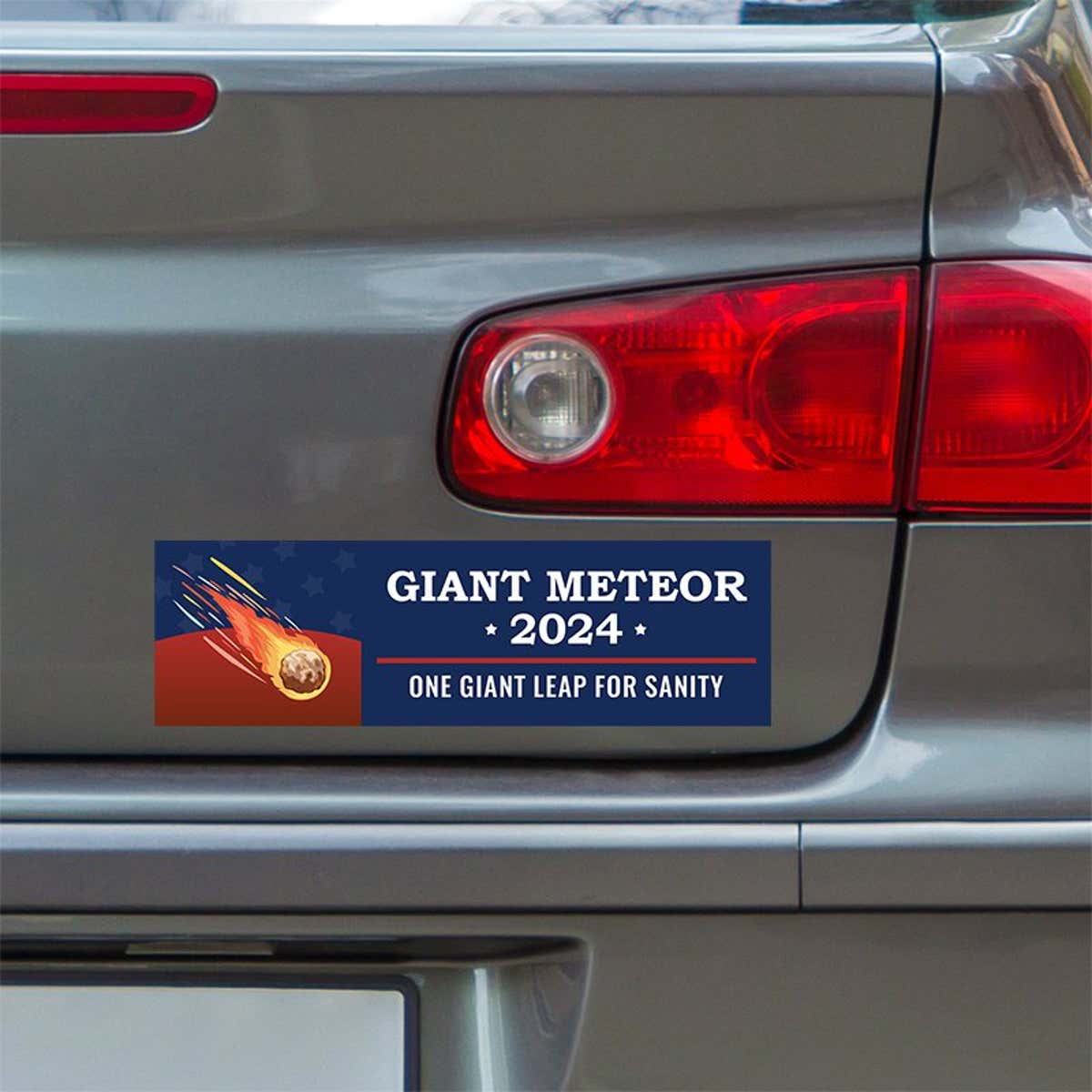 Giant Meteor Bumper Sticker below a gray car's tail light