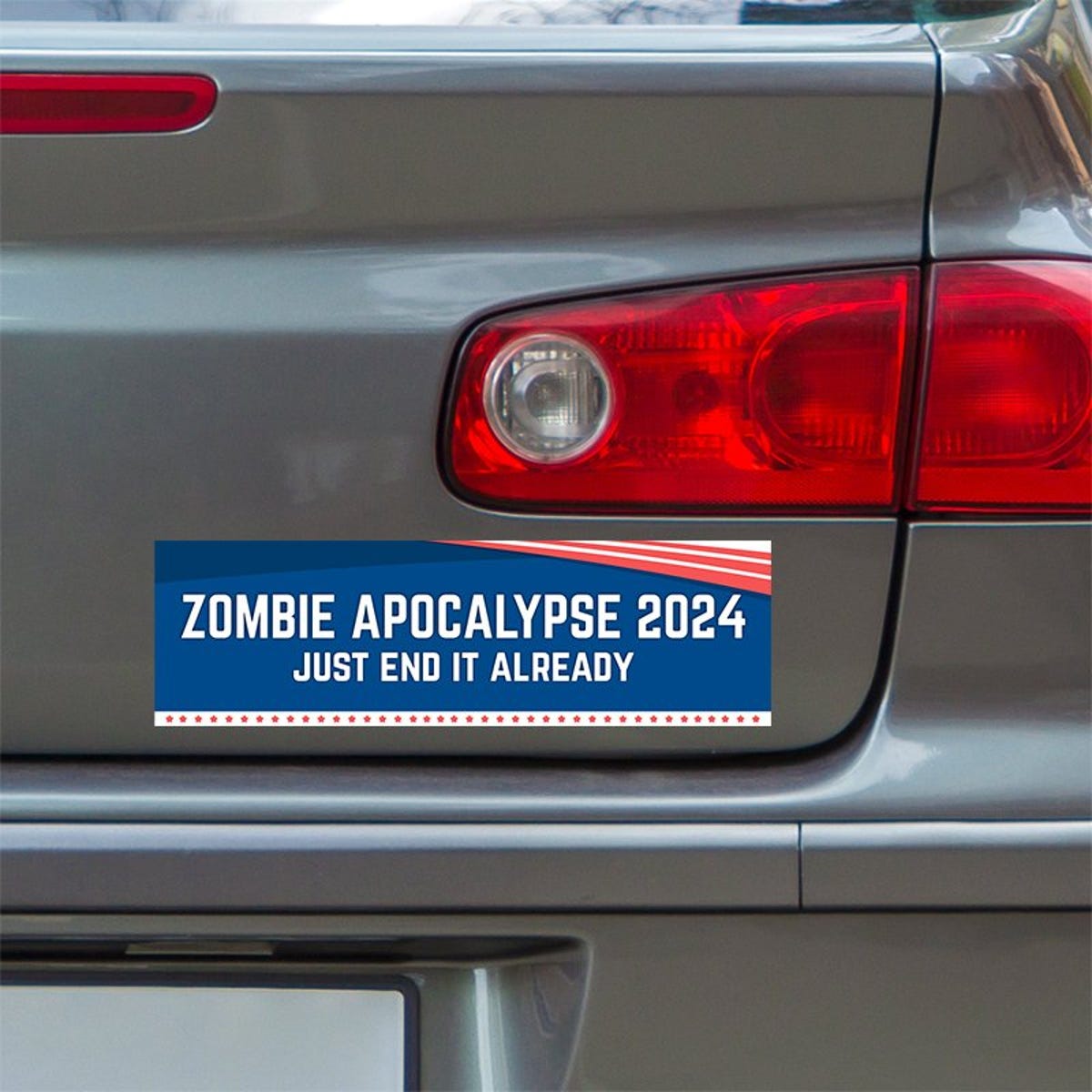 Zombie Apocalypse Political Bumper Sticker below a gray car's tail light