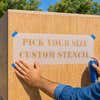 A stencil being secured onto a wooden box using painters tape