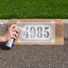 A person spray painting numbers onto a curb using a stencil