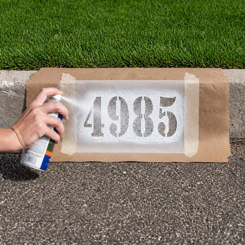 A person spray painting numbers onto a curb using a stencil